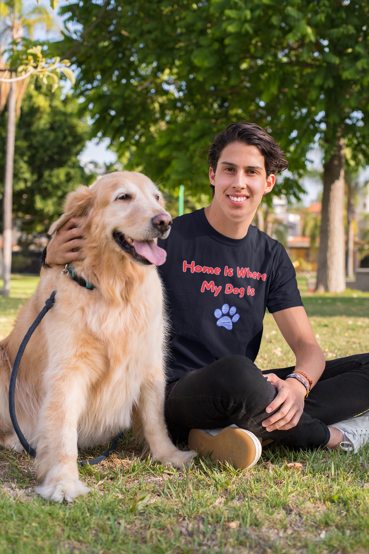 Man sitting on the grass with his golden retriever, wearing the Home Is Where My Dog Is tee