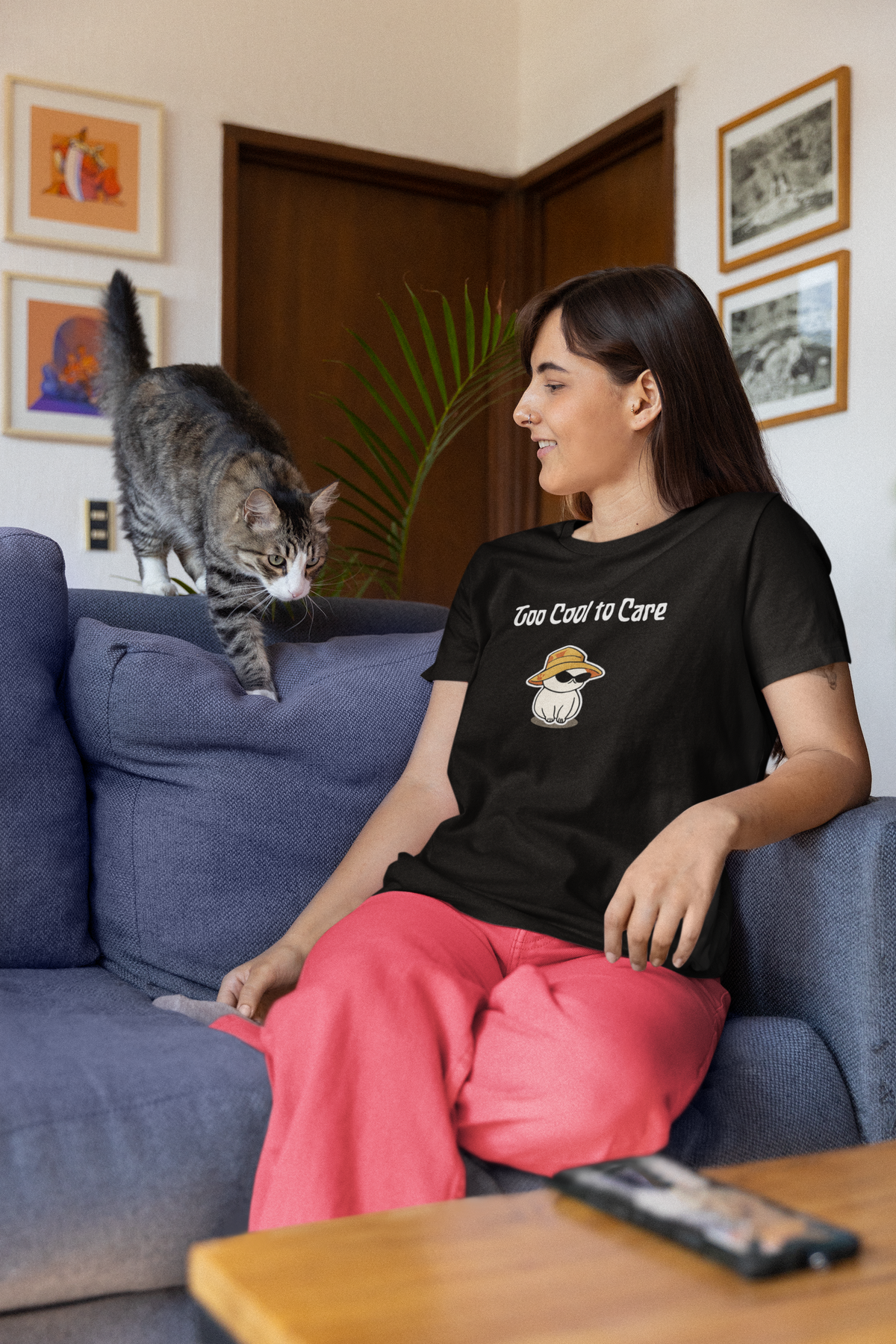 Woman relaxing on the couch with her cat, wearing the Too Cool To Care tee
